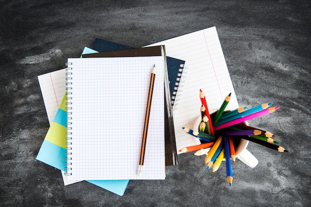 School supplies on black board background. Color pencils, calculator, rules and copybooks. Back to school concept. 