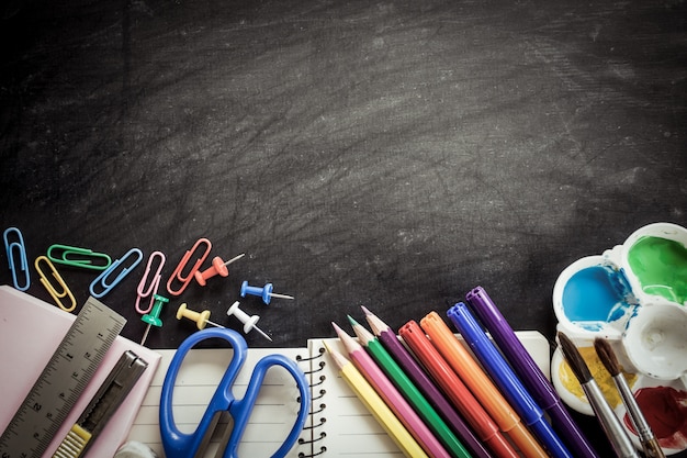 School supplies on blackboard background in dark tone