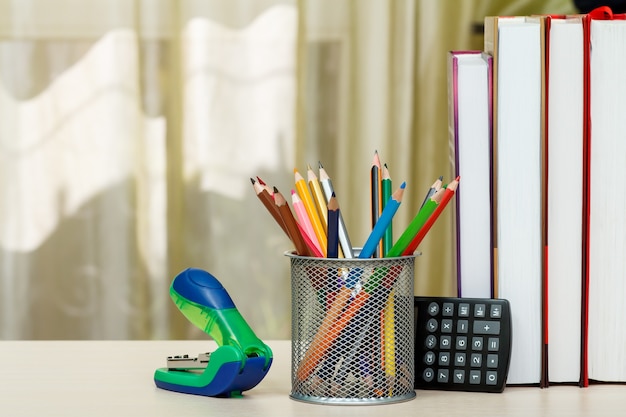 School supplies. Books, colour pencils, calculator, stapler on wooden table. Back to school concept