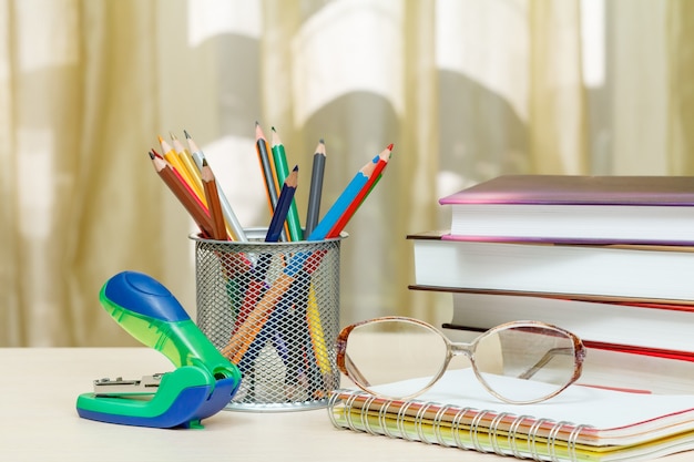 School supplies. Books, colour pencils, glasses, notebook, stapler on wooden table. Back to school concept