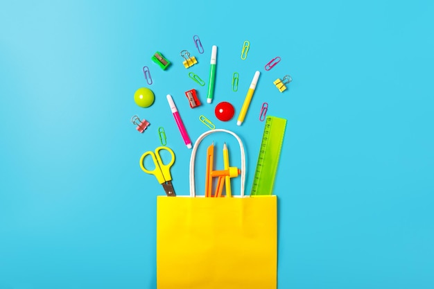 School supplies in a bright yellow paper bag on a blue
background back to school concept concept of shopping in a
stationery store school sale concept top view flat lay