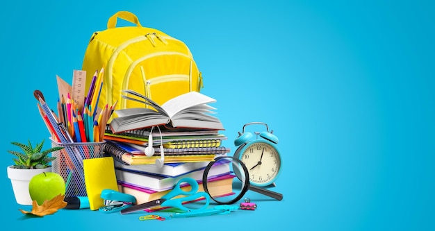 school supplies composition with yellow school bag on turquoise blue background copy space