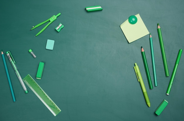 School supplies on empty green chalk board top view Back to school