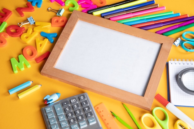 school supplies and frame on orange background