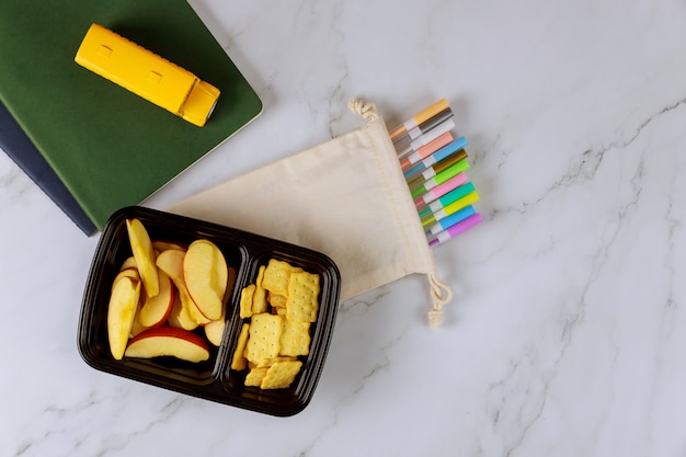 Foto materiale scolastico e lunch box con fette di mela e cracker