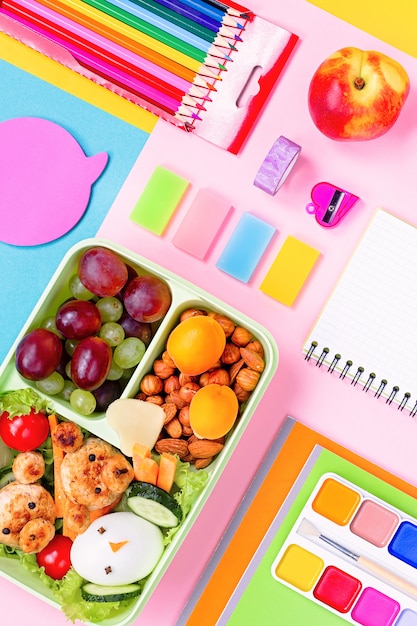 Foto materiale scolastico e lunchbox con cibo per bambini. disposizione variopinta della cancelleria su superficie multicolore, spazio della copia
