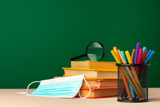 School supplies and medical face mask on desk, copy space