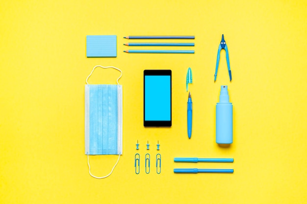 Photo school supplies and mobile phone on yellow background back to school in pandemic concept