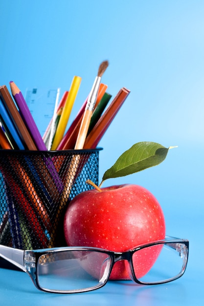  School supplies pencils, pens, ruler, brush, books and apple on blue background 