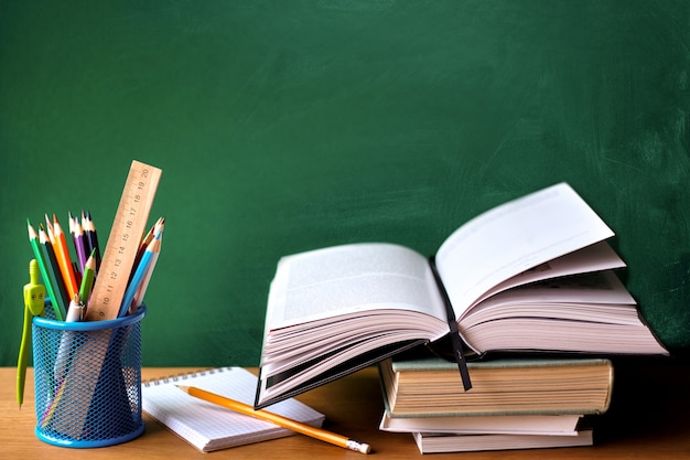 School supplies, stack of books, chalkboard and open book on a wooden surface