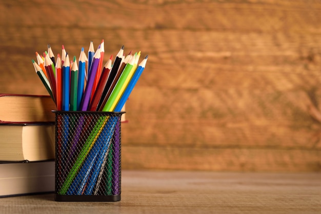 School supplies on a warm, beautiful wooden background. Colored children's pencils in a locker black holder for stationery.