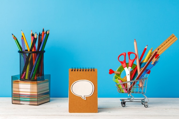 School supplies on wooden desk against blue background, front view