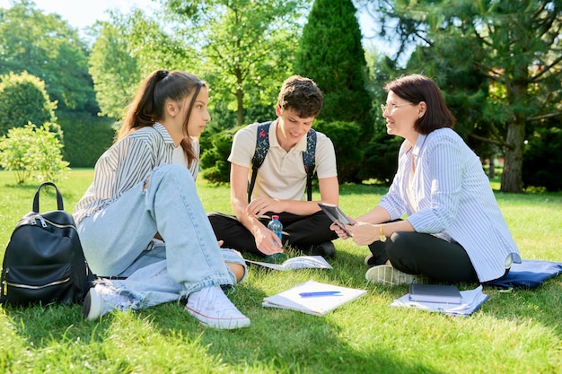 School teacher psychologist social worker talking to teenagers sitting on grass