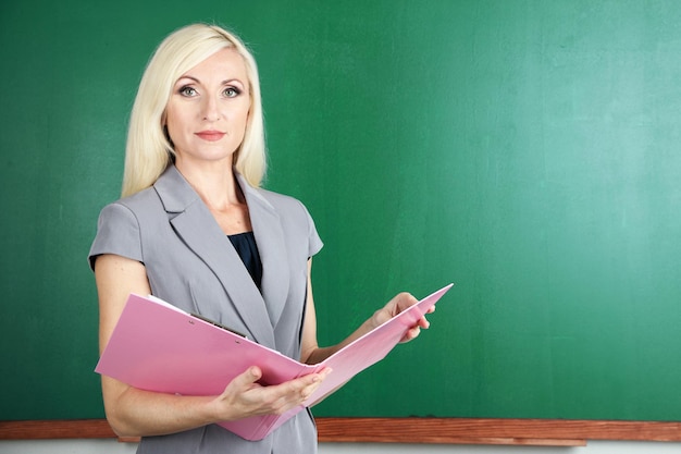 School teacher with folder near blackboard closeup