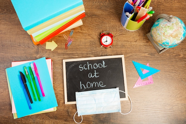 Foto school thuis inscriptie met krijt op een klein schoolbord. bureau met schoolaccessoires en een beschermend masker, bovenaanzicht, flat lay