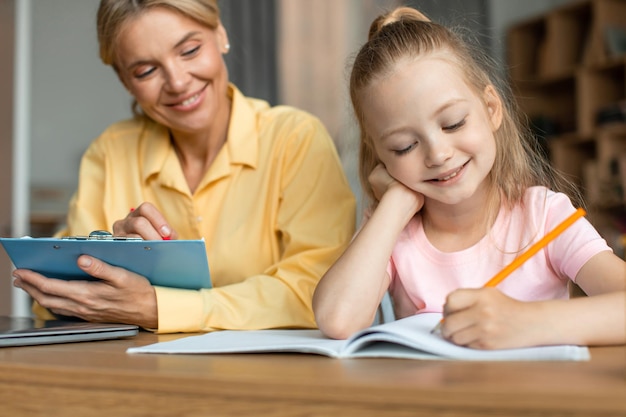 School voor kinderontwikkeling Professionele vrouwelijke taalleraar die traint met een slim kind van een meisje dat in het schrijfboek schrijft