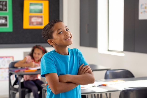 In school young biracial boy standing with arms crossed looking thoughtful in the classroom