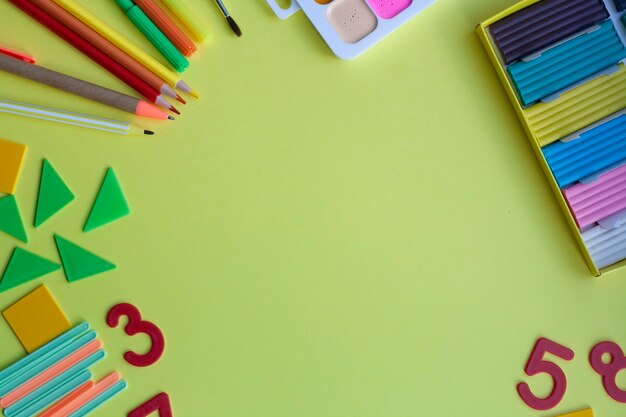 Schoolachtergrond met schoolbenodigdheden op geel, pen, potloden, stiften, aquarellen, plasticine, puntenslijper, getallen, geometrische vormen, telstokken, plat leggen, kopieerruimte