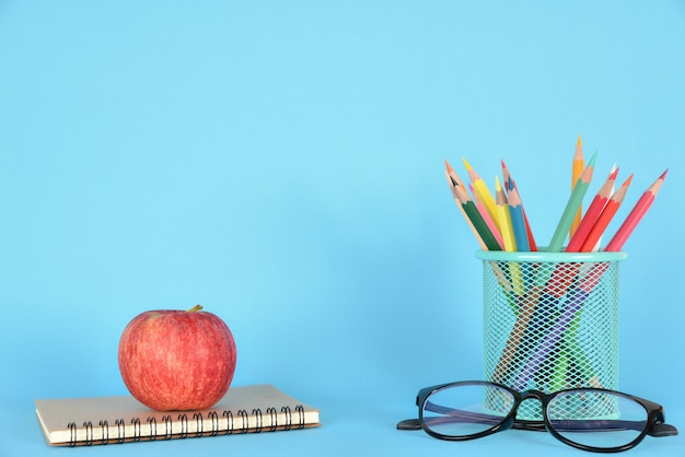 Schoolbenodigdheden, appel, glazen en boek op blauw