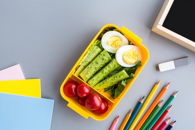 Schoolbenodigdheden en lunchbox met sandwich en groenten