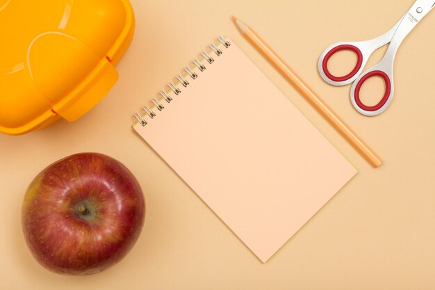 Schoolbenodigdheden Lunchbox apple notebook kleurpotlood en schaar op beige achtergrond Bovenaanzicht