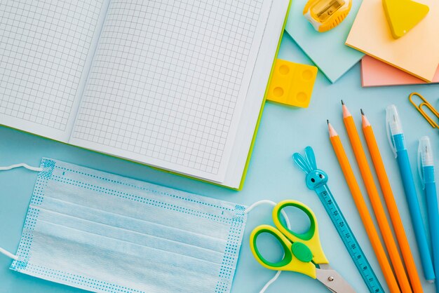 Schoolbenodigdheden met medisch gezichtsmasker op blauw, bovenaanzicht