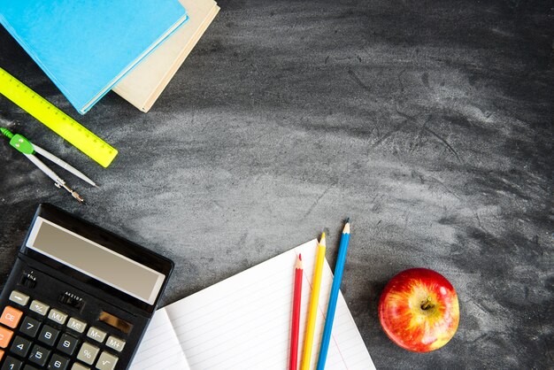 Schoolbenodigdheden op zwarte bord achtergrond. kleurpotloden, rekenmachine, regels en voorbeeldenboeken. terug naar school-concept.