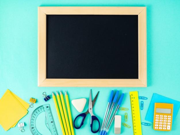 Schoolbord, schoolbenodigdheden op witte tafel, blauwe muur.