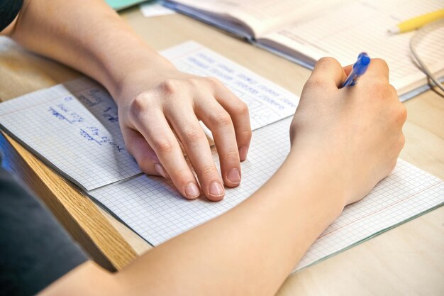 Schoolboy in black tshirt does homework sitting at wooden desk at home close view