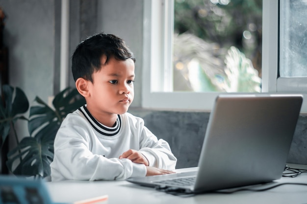 Schoolboy boy studies online on a laptop at home. Communicates online with a teacher. Teaches lessons from school at the computer. Participates in distance education.