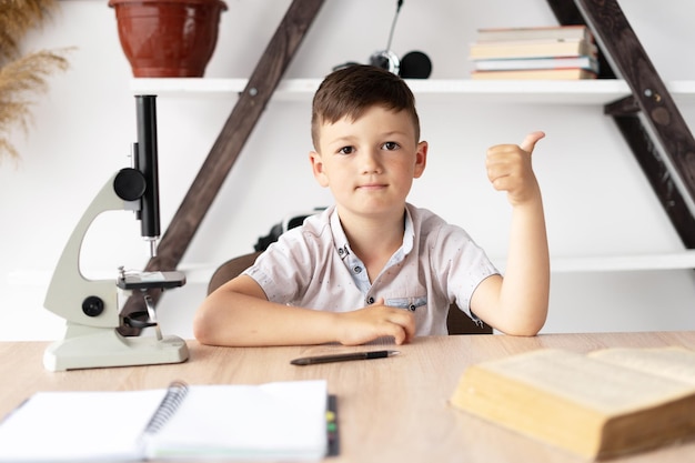 Schoolboy boy studying at home at the desk has a biology lesson and a microscope Online education and home tutoring Pupil receives knowledge remotely Closeup