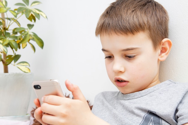 Schoolboy boy with a phone in his hands. Communication or study with a smartphone. Distance learning online.