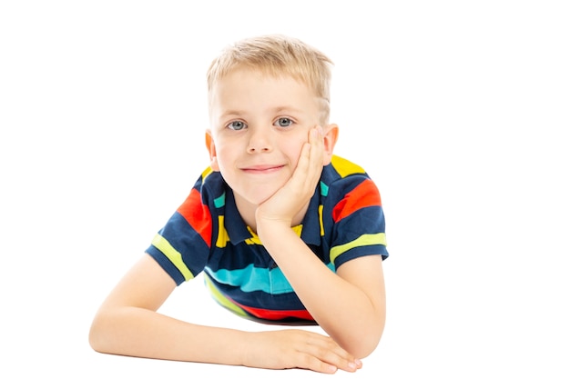 A schoolboy in a bright striped sweater is lying on the floor and smiling. Isolated over white background.