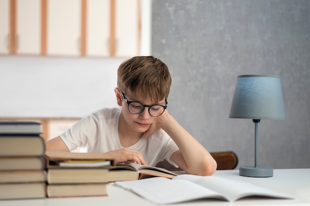 안경을 쓴 남학생이 숙제를 합니다. 원격 교육. 소년은 교과서를 읽습니다. 홈스쿨링