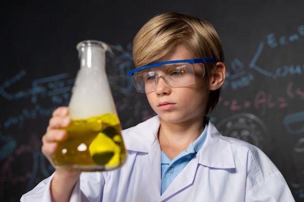 Photo schoolboy in laboratory stem class wear lab coat hold yellow liquid erudition