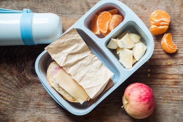 Schoolboy lunch box with thermos on wooden backgroundappletangerinesandwich in lunchbox and water bottle