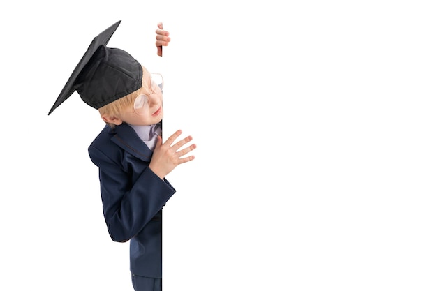 Schoolboy peeking out from behind white board Space for text Boy in school uniform big glasses and student hat Copy space