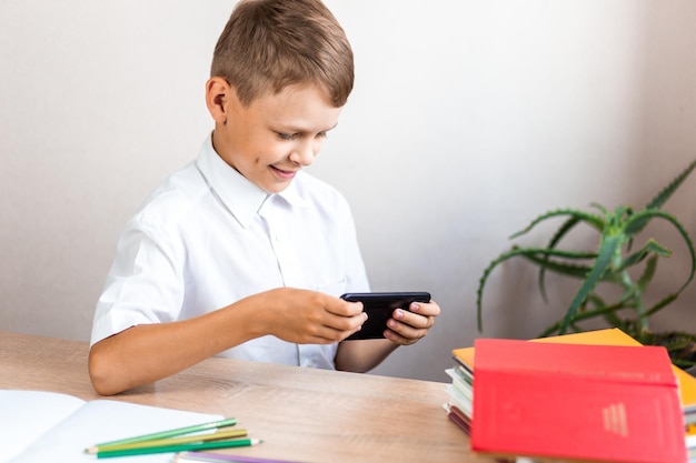 Schoolboy playing on the phone while sitting at his desk