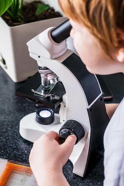 実験室の顕微鏡を使った男子学生の研究者、科学実験室の子供のコンセプト。科学教育