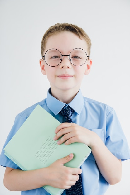 Schoolboy in school uniform and glasses holding a stack of notebooks in his hands