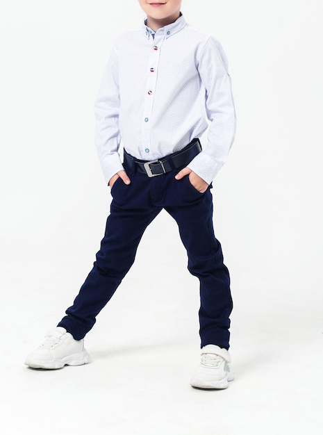 Schoolboy in a school uniform on a white background The boy demonstrates a shirt trousers a belt and sneakers Vertical photo