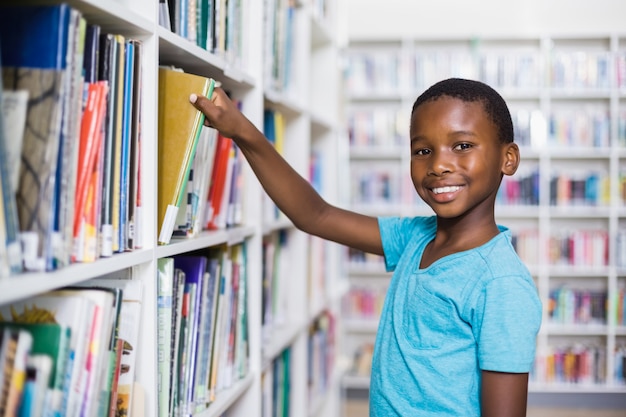 Schoolboy selecting a book from bookcase in library