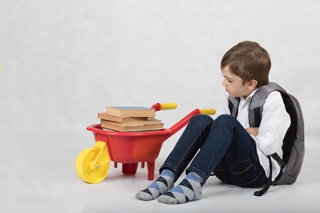 本でいっぱいのプラスチック製の手押し車を持った 7 歳の男子生徒。テキスト用の空き領域。