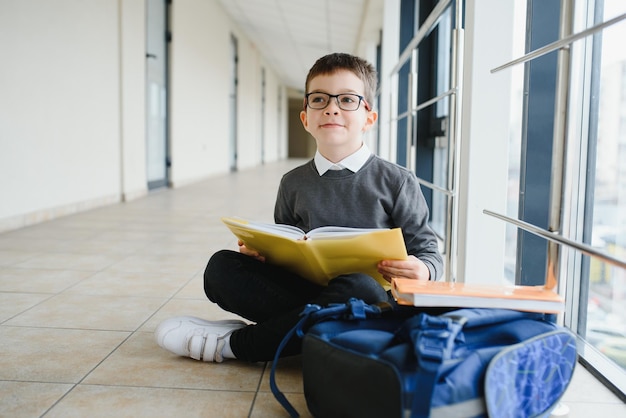 Schoolboy sits on the floor of a school hallway and reads a book