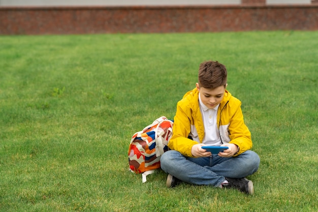 Schoolboy sits on the lawn with smart phone