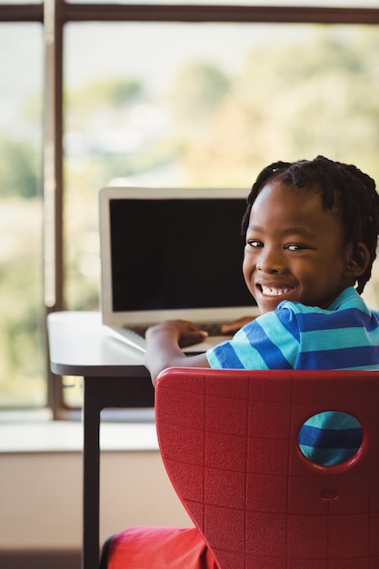 Schoolboy sitting on chair and using laptop at school