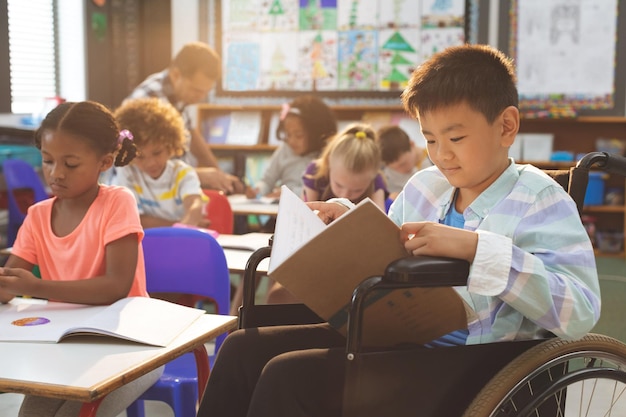 Schoolboy studying in classroom while sitting at wheelchair