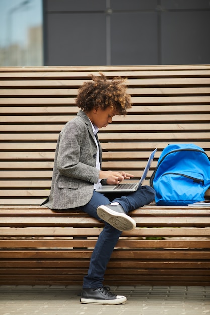 Schoolboy typing on laptop outdoors