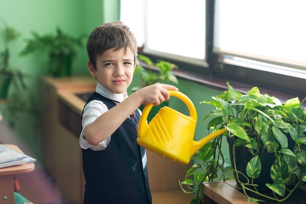 Scolaro che innaffia i fiori da un annaffiatoio giallo in classe