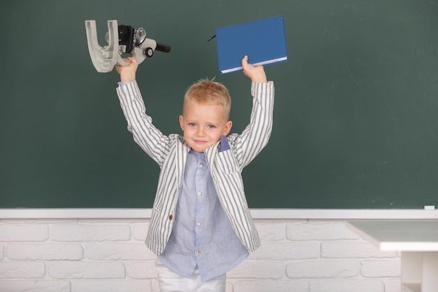 小学校の教室の授業で数学を勉強している顕微鏡と本を持った男子生徒